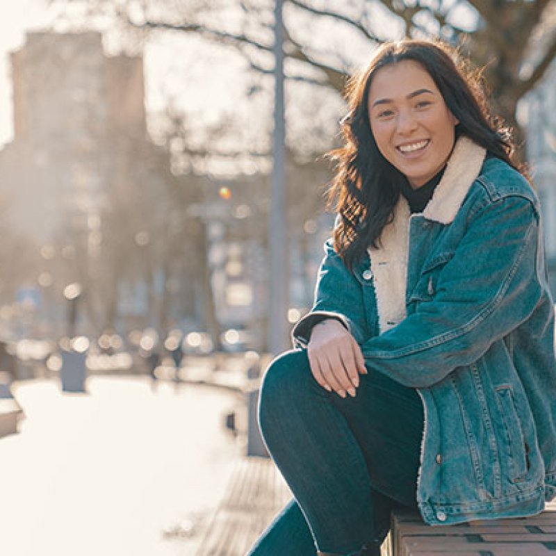 Girl sitting on a wall in a city park on a sunny day smiling at the camera.jpg